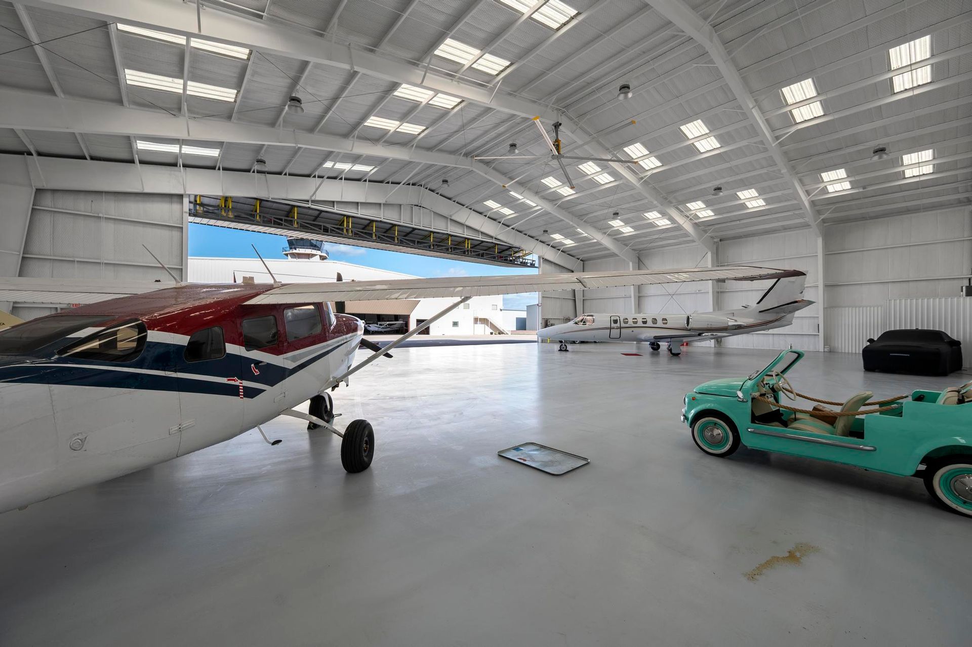 Small airplane and green utility vehicle inside a bright aircraft hangar.