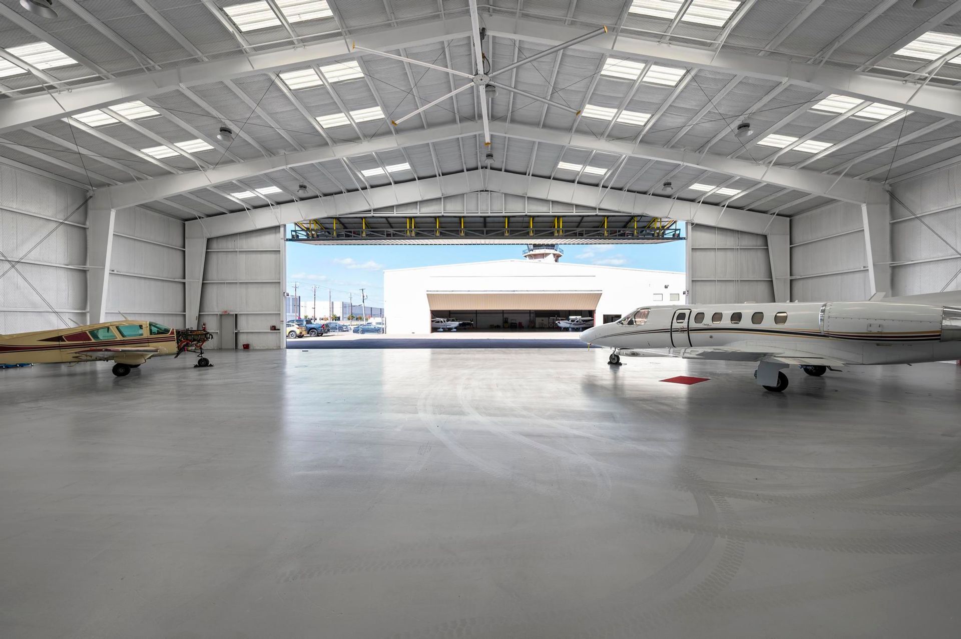 Empty aircraft hangar with two small planes inside and large open doors showing daylight outside
