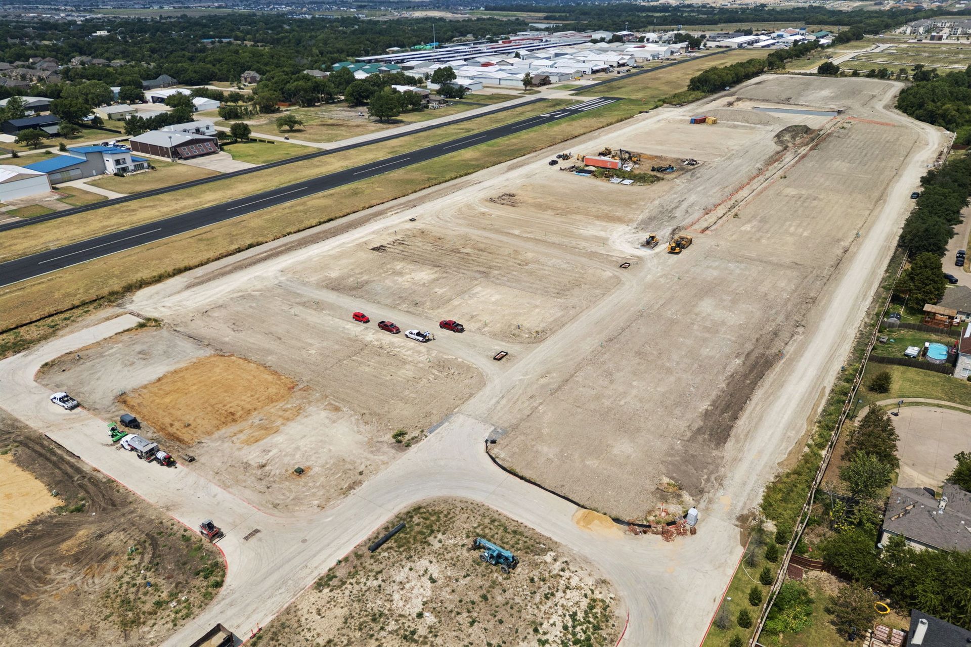 Aerial view of a large dirt construction site beside a road and buildings