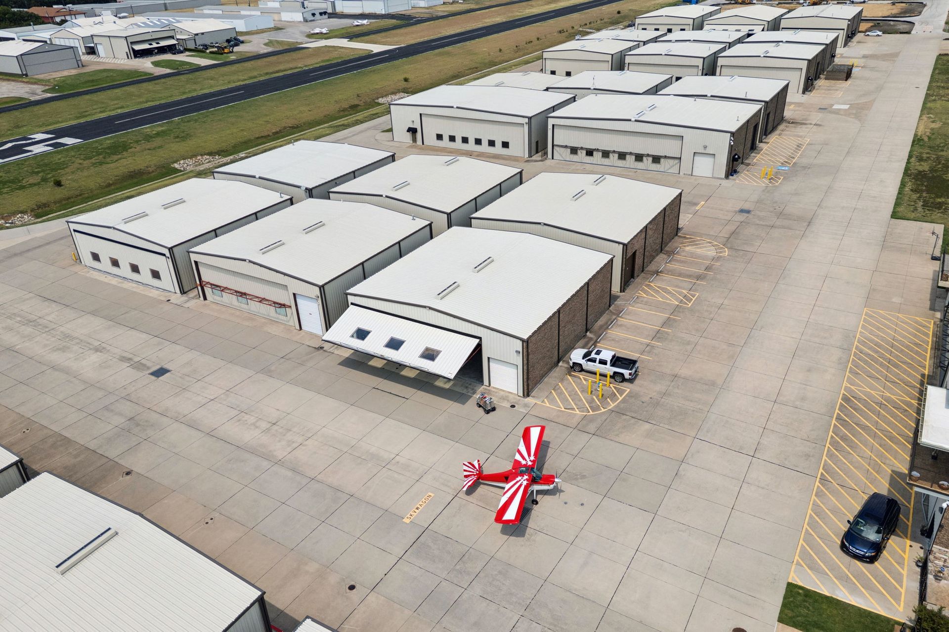 Aerial view of a red-and-white small airplane parked on a concrete apron beside hangars.