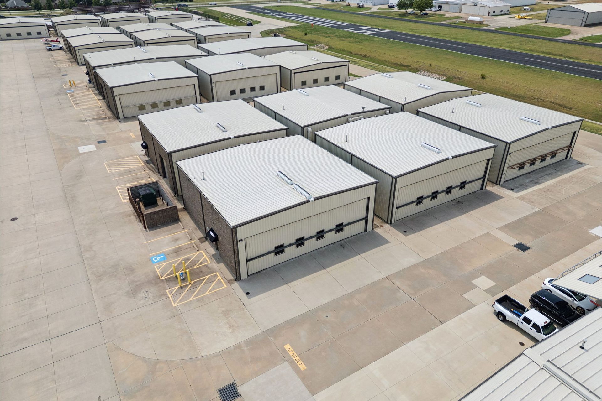 Aerial view of beige industrial warehouse buildings and parking lots near a road.