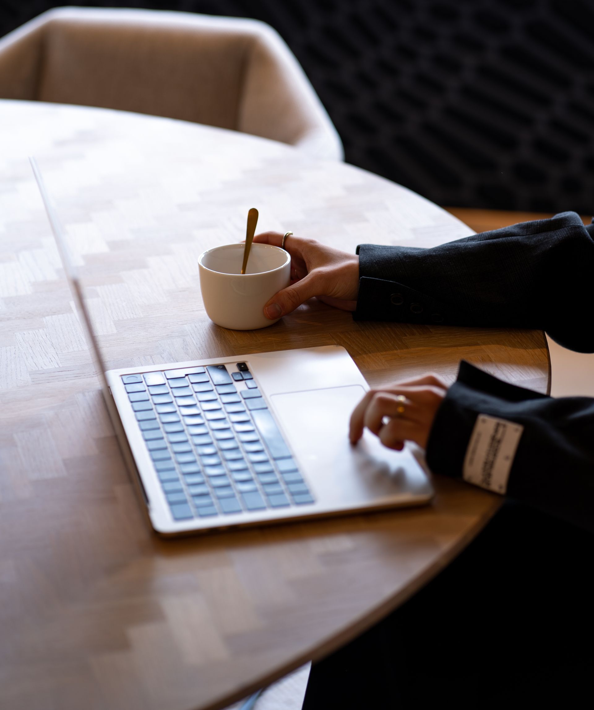 Een persoon typt op een laptop terwijl hij een kopje koffie vasthoudt