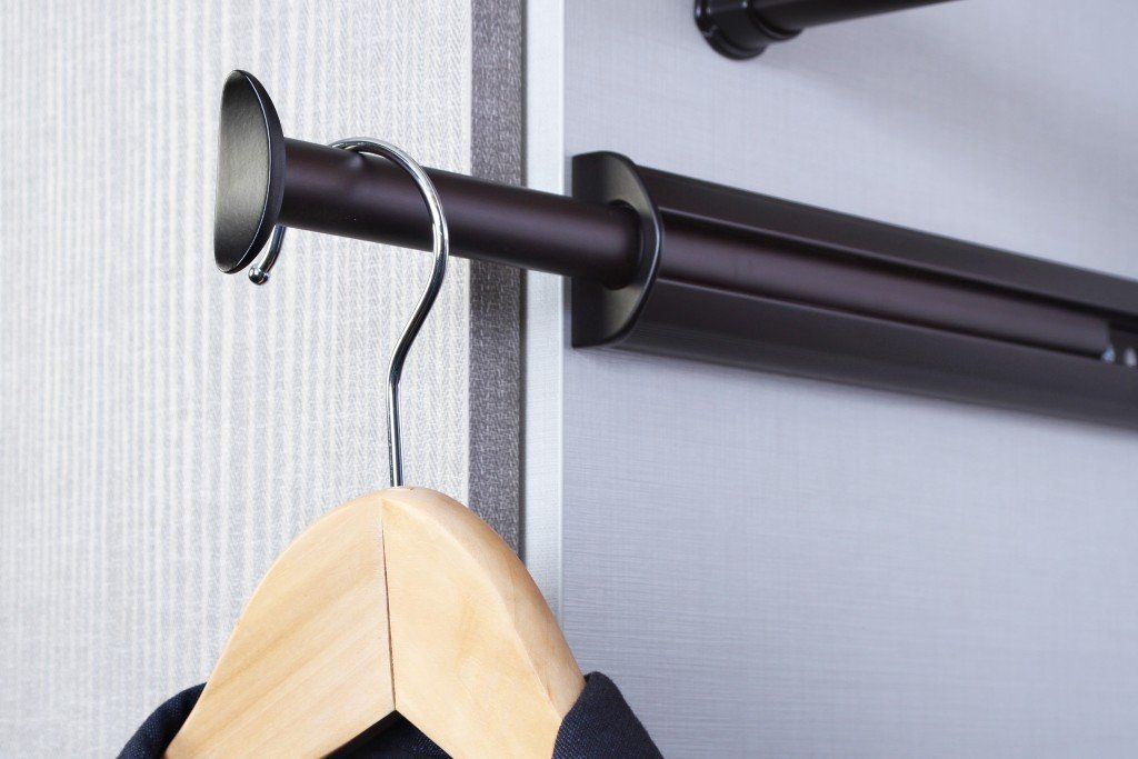 A wooden hanger is hanging on a metal rail in a closet.