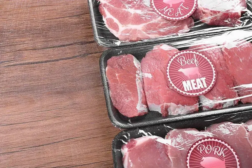 Three Trays of Raw Meat With Labels on Them on a Wooden Table — Aldine Printers in Bungalow, QLD