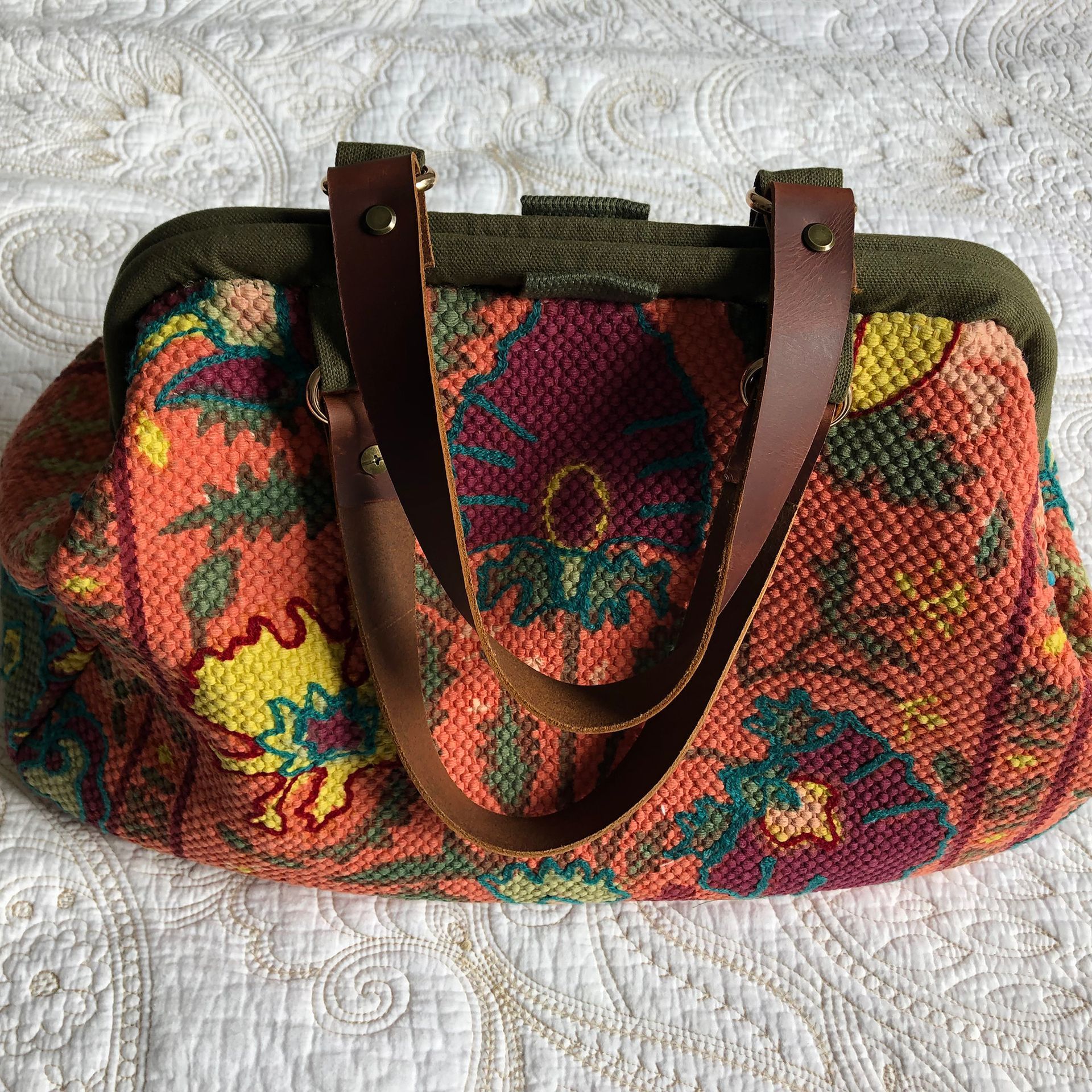 Orange floral print handbag with brown leather handles on a white bedspread.