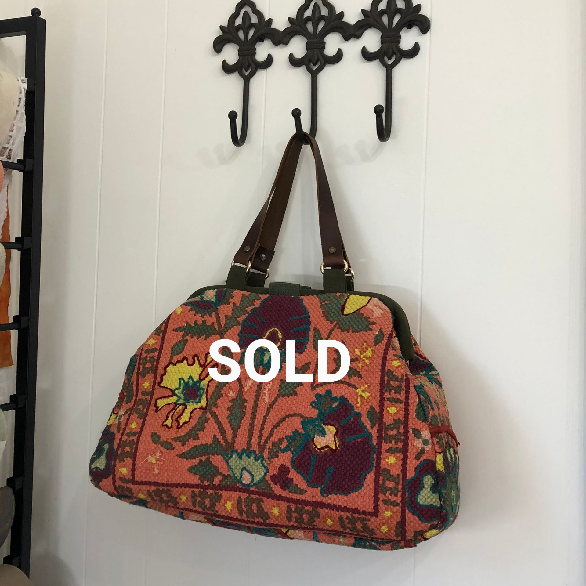 Orange floral tote bag hanging on a black metal hook on a white wall.