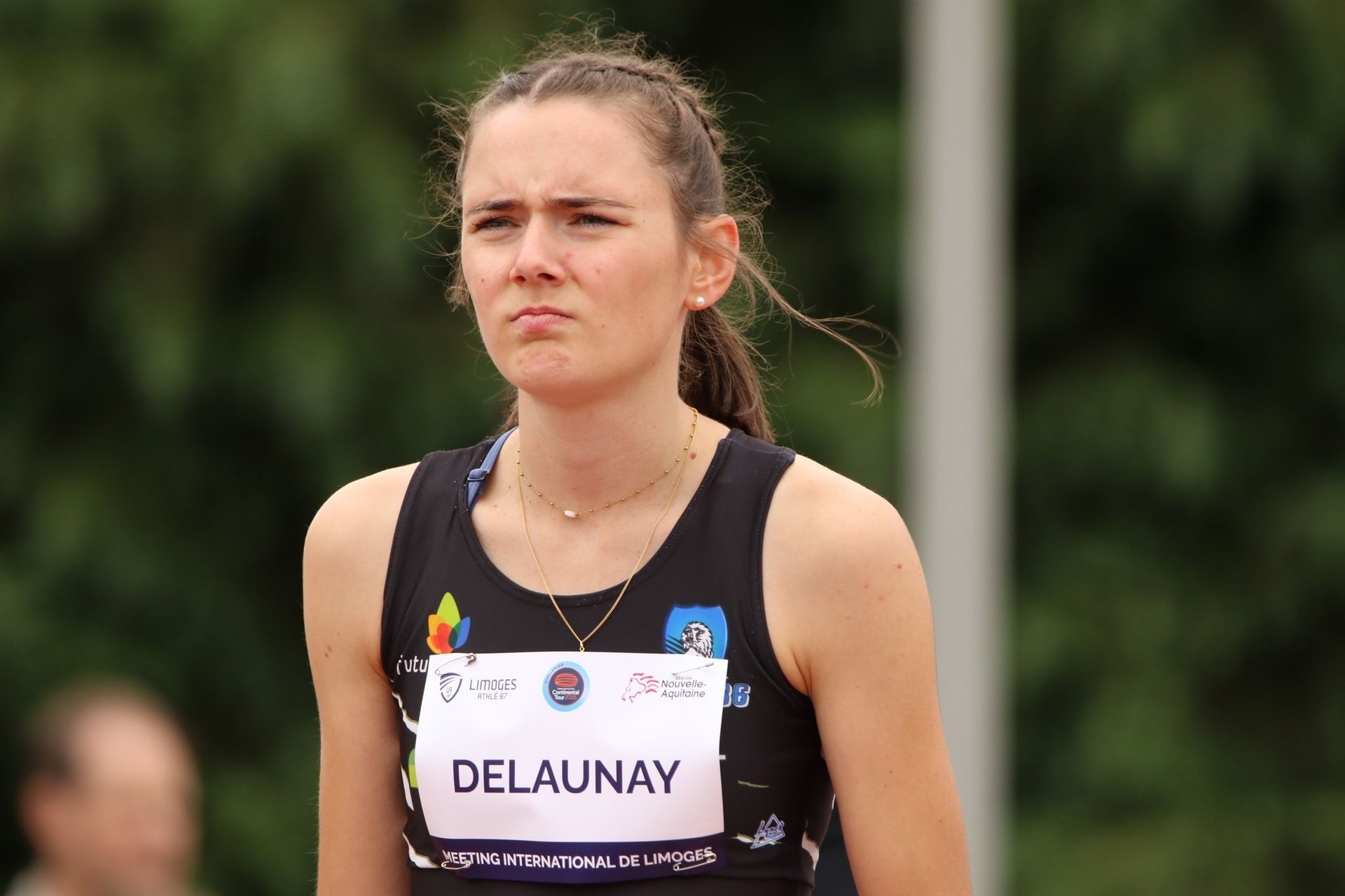 L'athlète féminine, Diane Delaunay, en uniforme d'athlétisme, l'air déterminée sur un terrain d'athlétisme.