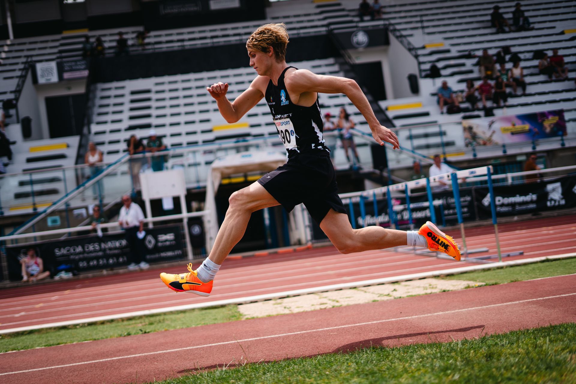 Sauteur en longueur masculin en uniforme EPA86, s'élance sur une piste, stade ensoleillé.