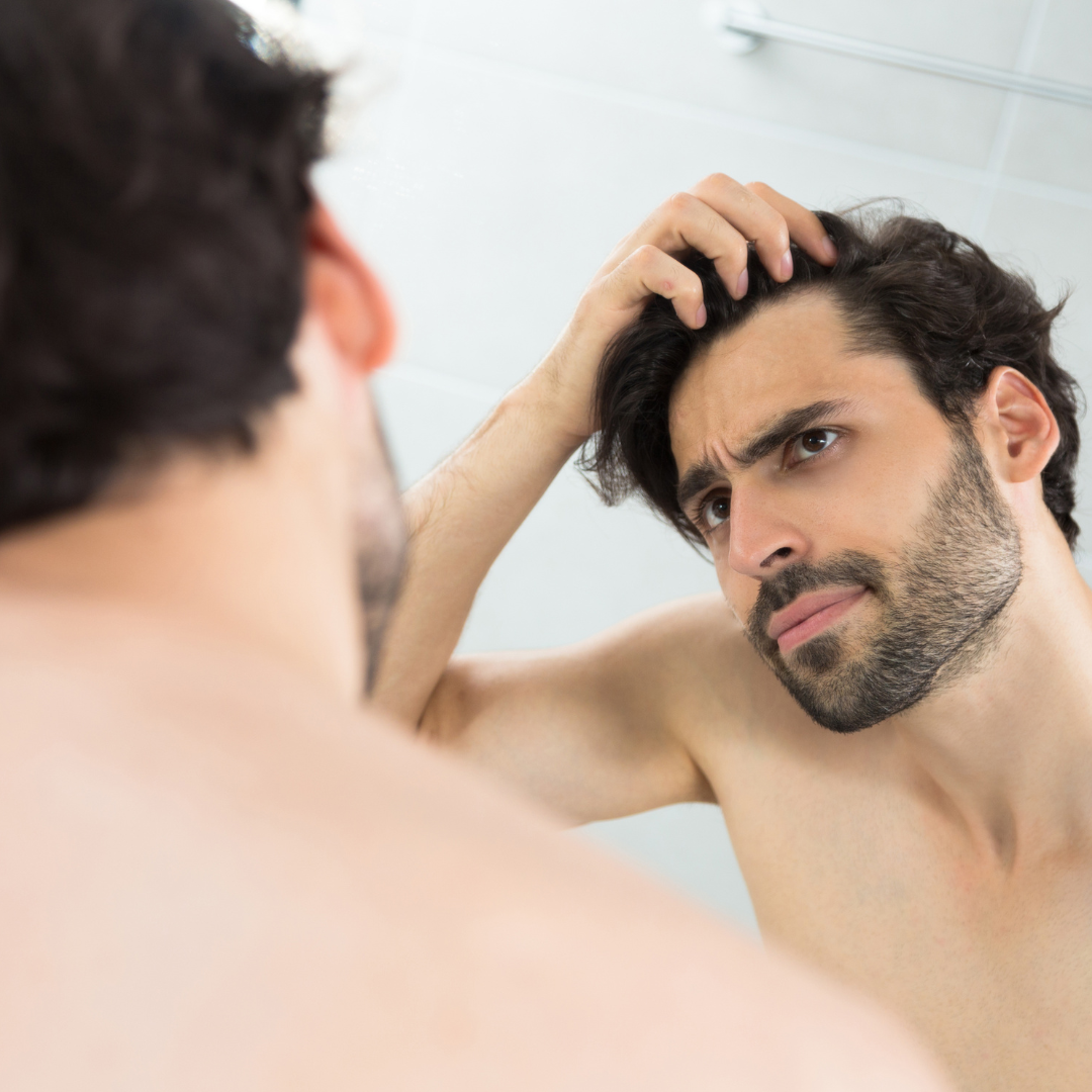 Man looking in the mirror, concerned, touching his hair in a bathroom.