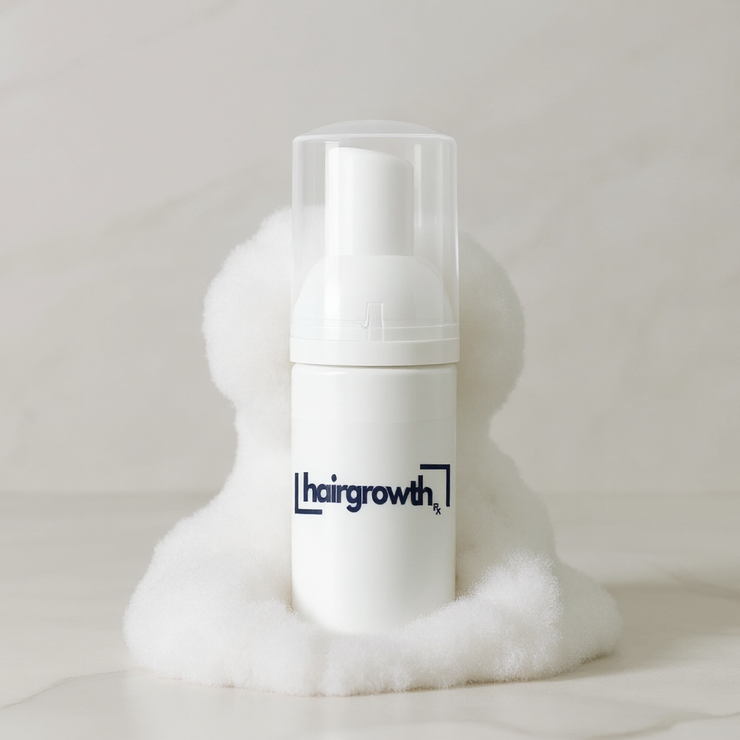 White hair growth foam bottle with a logo, held by fluffy white material.