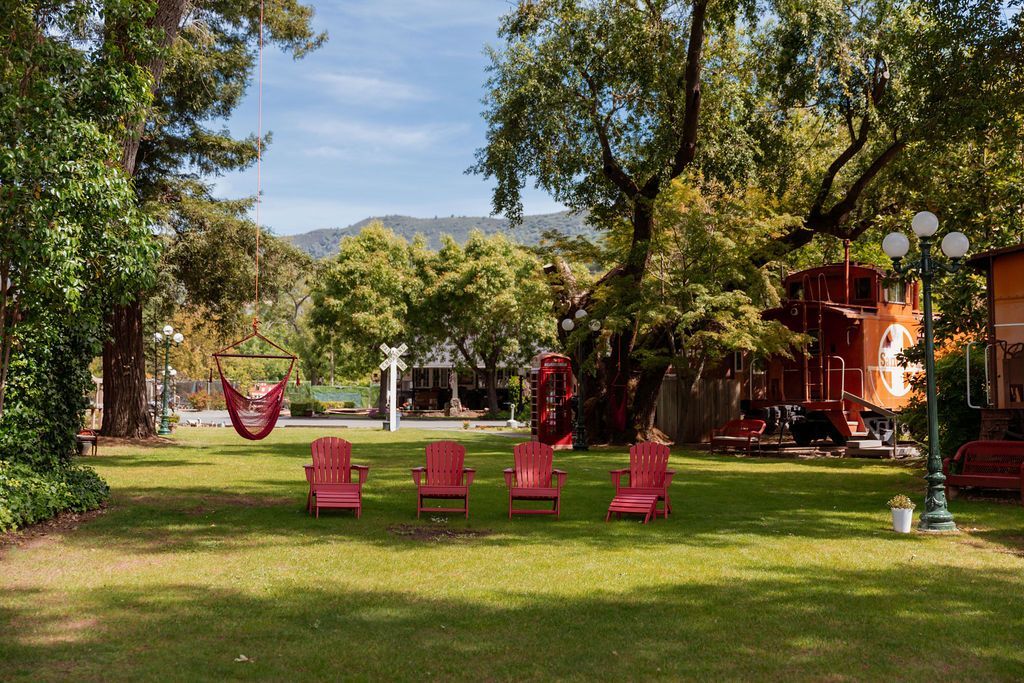 Sunny park with red chairs on a grassy lawn, trees, and a red building in the background