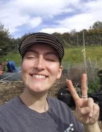 Smiling person in a striped cap making a peace sign outdoors under a cloudy sky