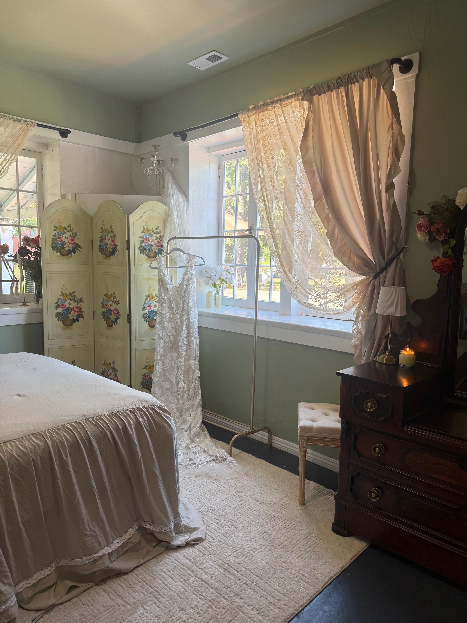Cozy bedroom with a bed, lace curtains, folding screen, and dark wood dresser by the window