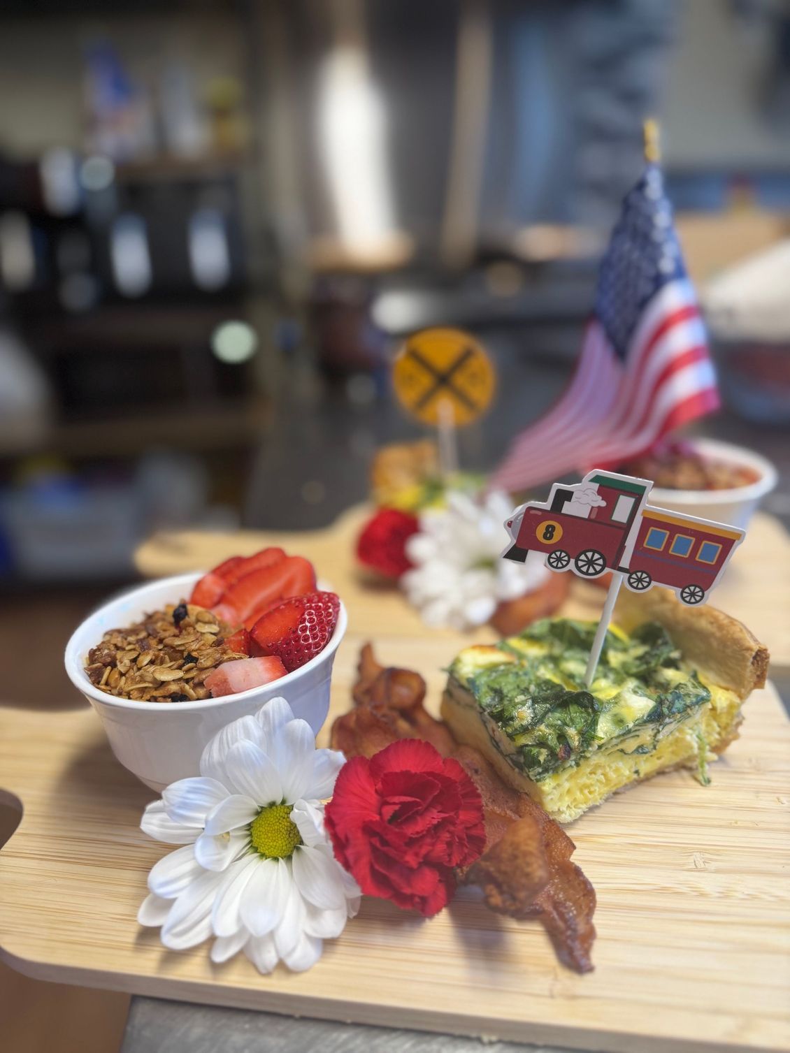 Dessert plate with cake, strawberries, bacon, flowers, and small American flags on a wooden board