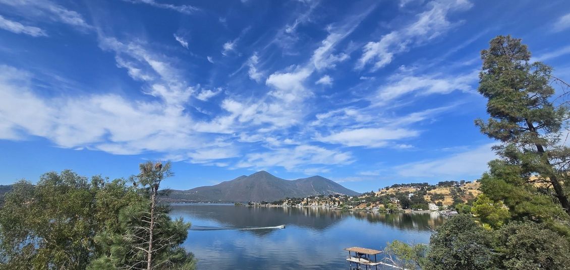 Mountain lake with a calm reflection, blue sky and clouds, framed by trees and distant hills