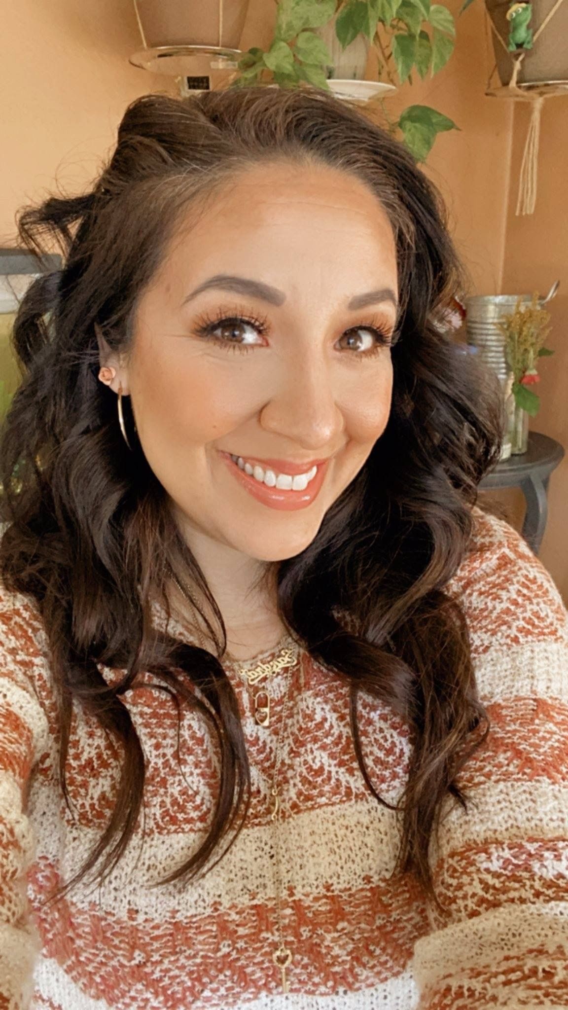 Smiling woman in a patterned sweater in a warm indoor setting with hanging plants