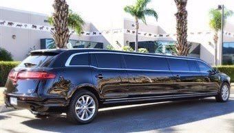 A black limousine is parked in front of a building with palm trees.