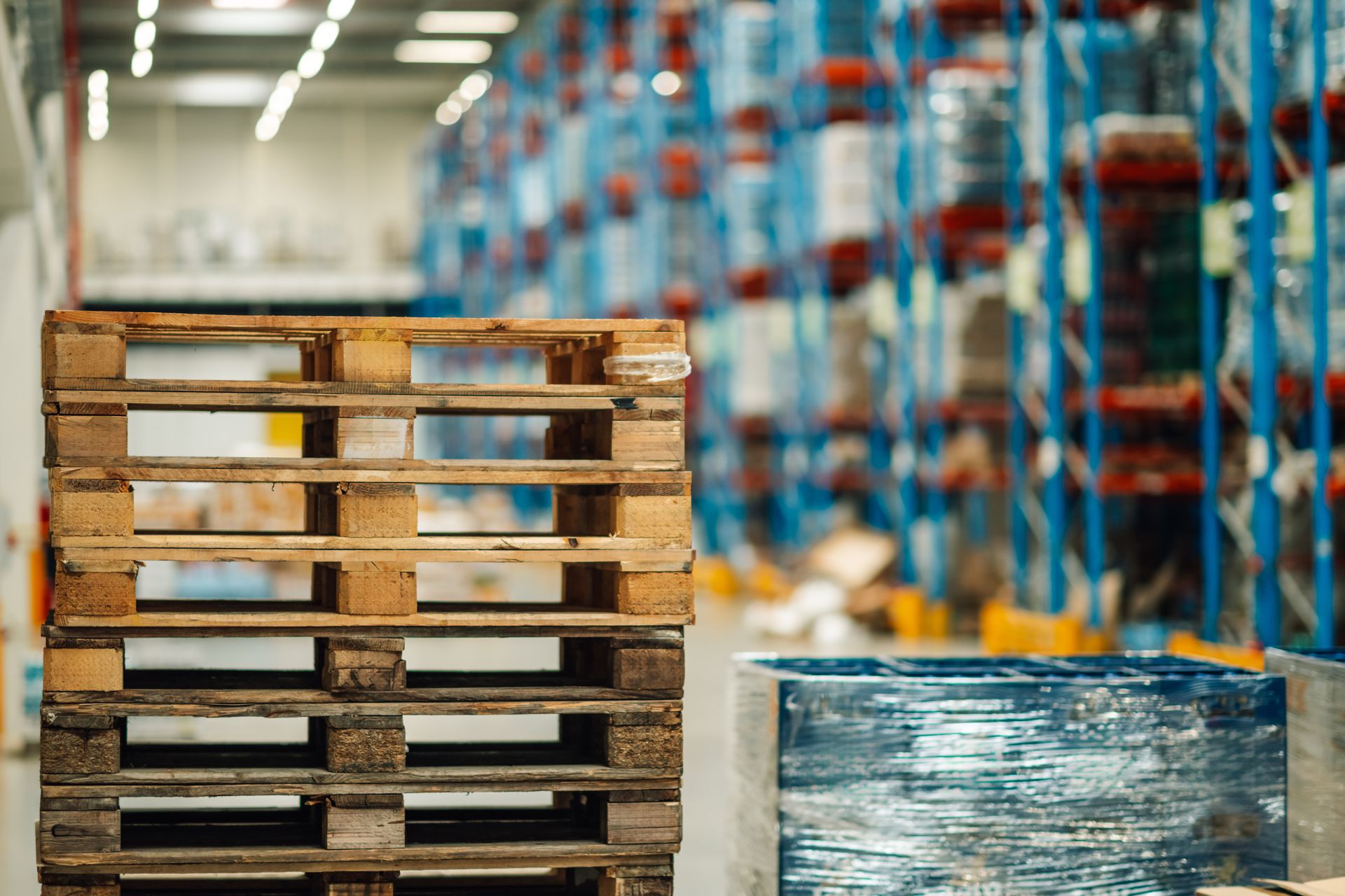 Wooden pallets stacked in a warehouse setting, shelves filled in the background.