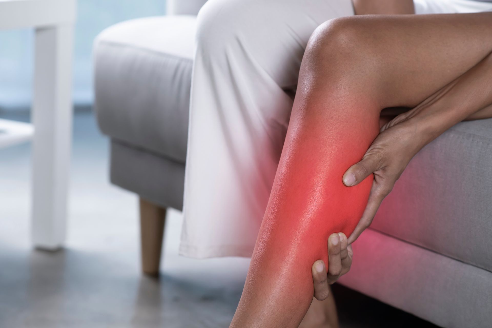 A woman is sitting on a couch holding her leg in pain.