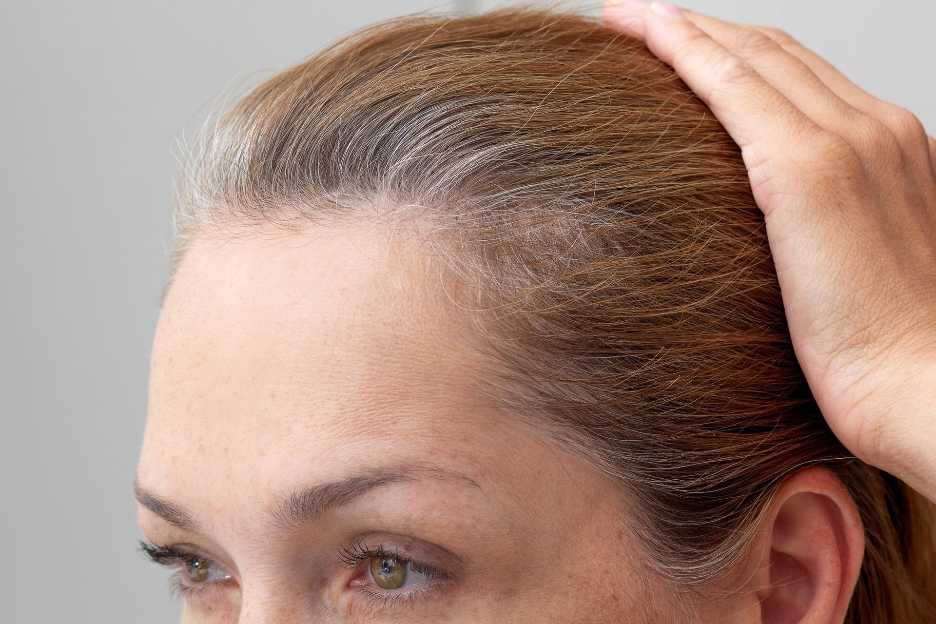 A woman is touching her hair with her hand.