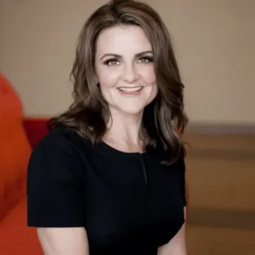 A woman in a black dress is smiling for the camera while sitting on a couch.