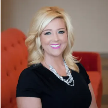 A woman in a black dress and necklace is smiling for the camera.