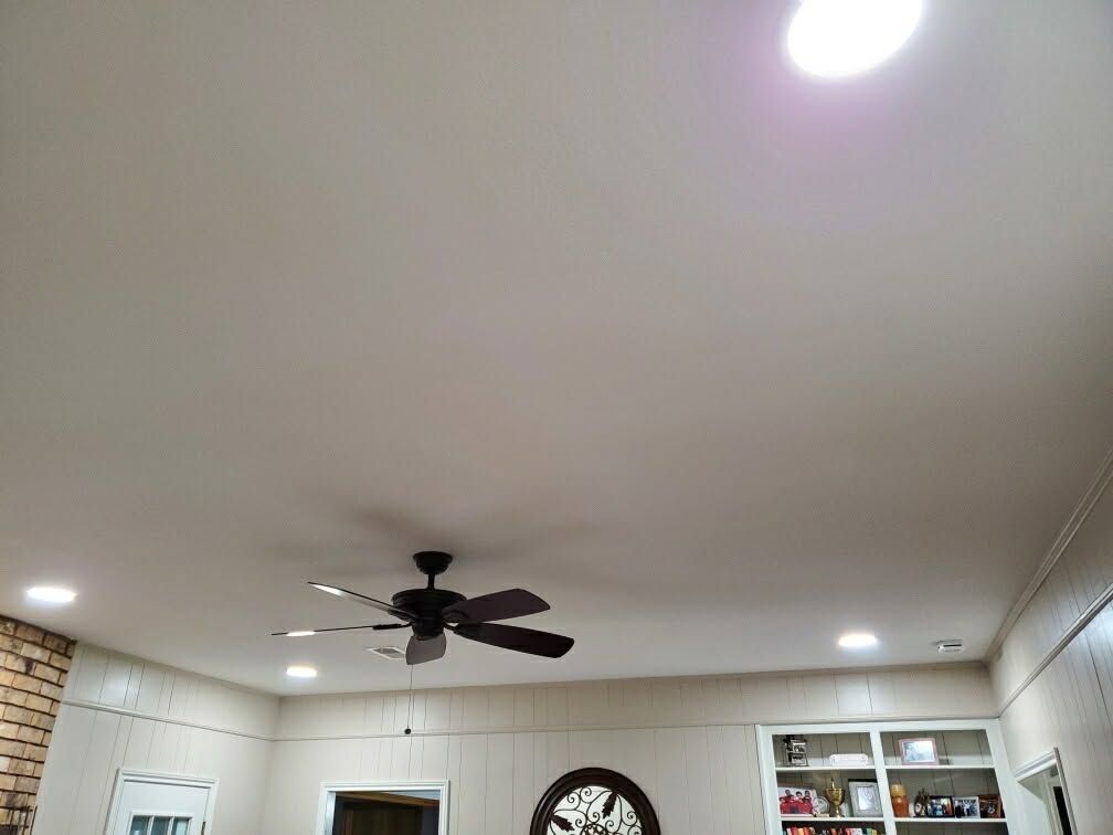Living room ceiling with a black fan, recessed lights, and a wall clock above white shelving