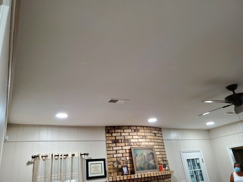 Living room with white ceiling lights, brick fireplace, wall art, and large windows with curtains