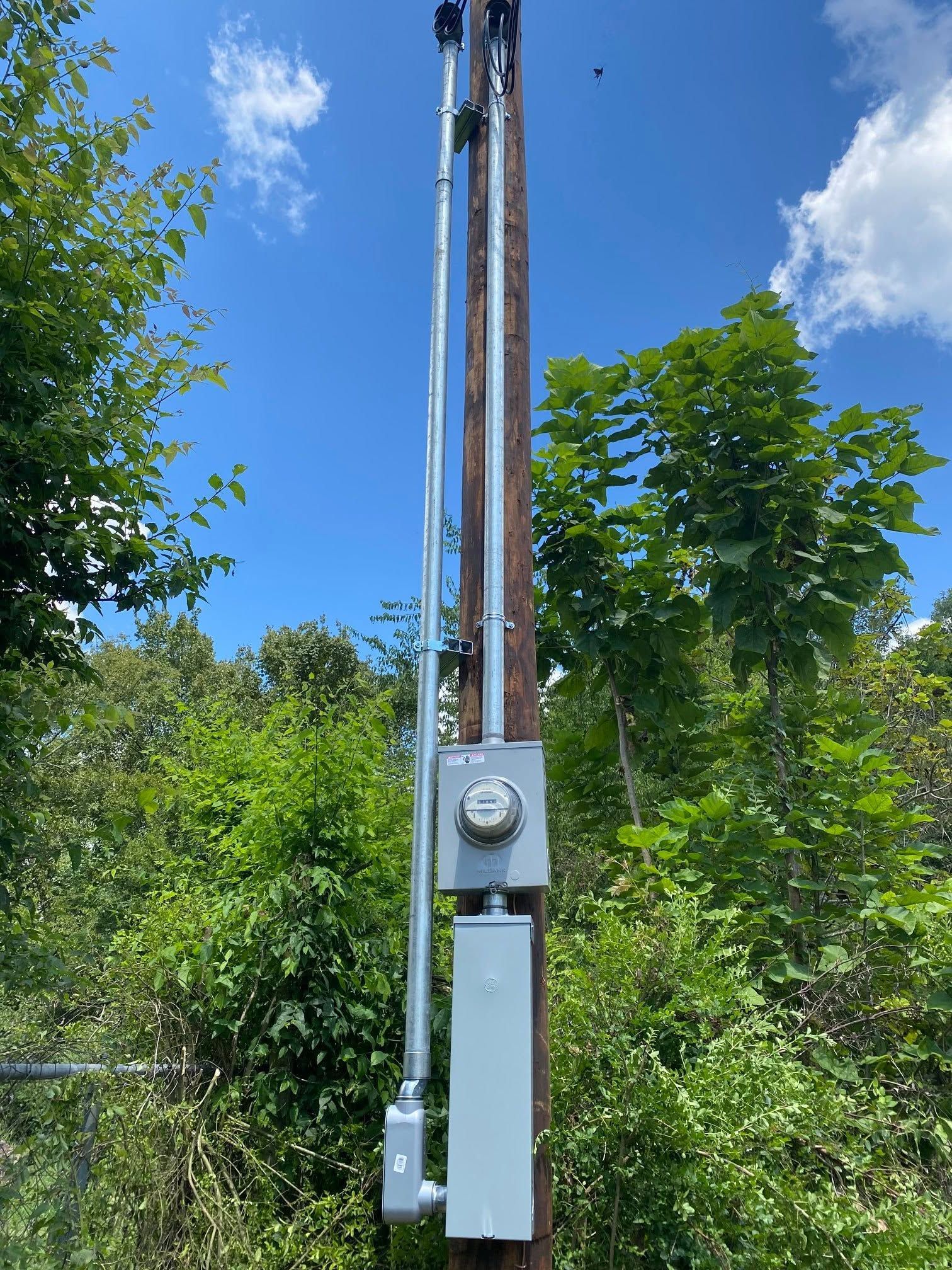 Utility pole with electrical equipment and wires against a blue sky and green trees