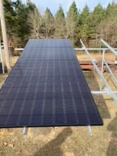 Large black solar panel array mounted outdoors on a metal frame, with trees in the background.