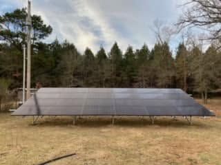 Solar panel array in a grassy field with trees in the background