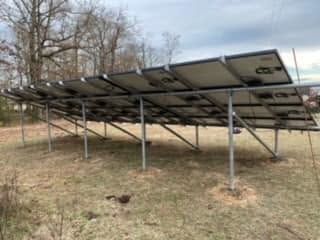 Ground-mounted solar panels in a grassy field with bare trees in the background
