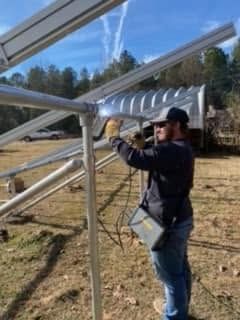 Worker using a power drill to assemble a metal frame outdoors under a clear blue sky