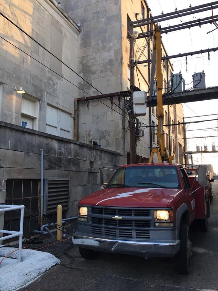 Red pickup truck parked in a narrow alley beside tall industrial buildings and scaffolding.
