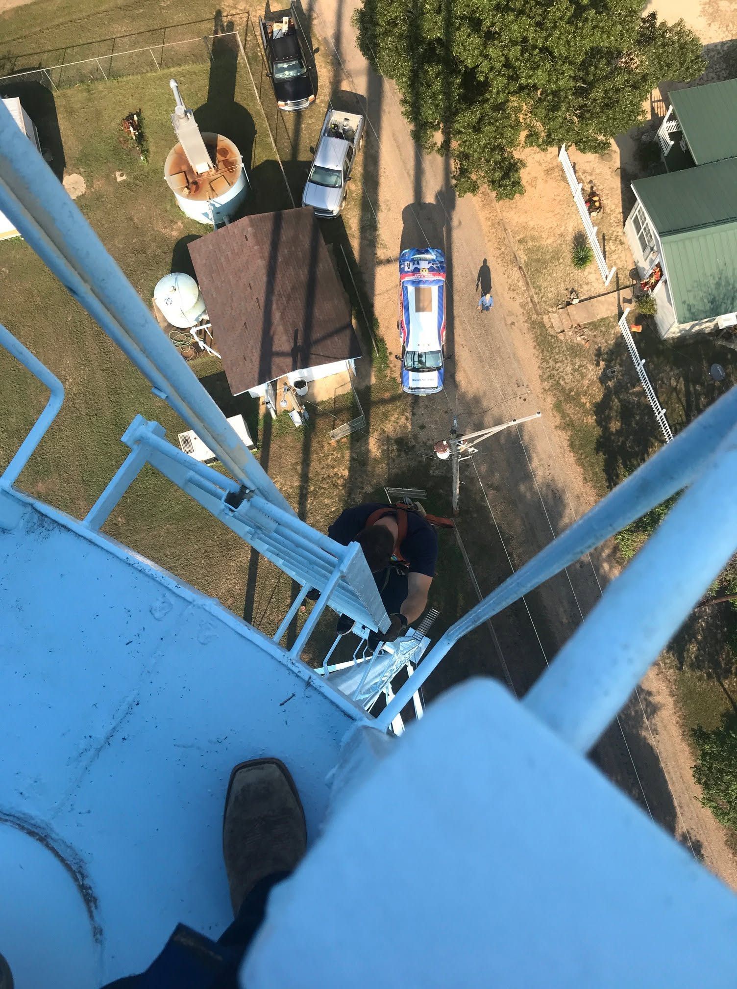 View from a blue tower looking down at a person on a narrow ladder and parked vehicles below