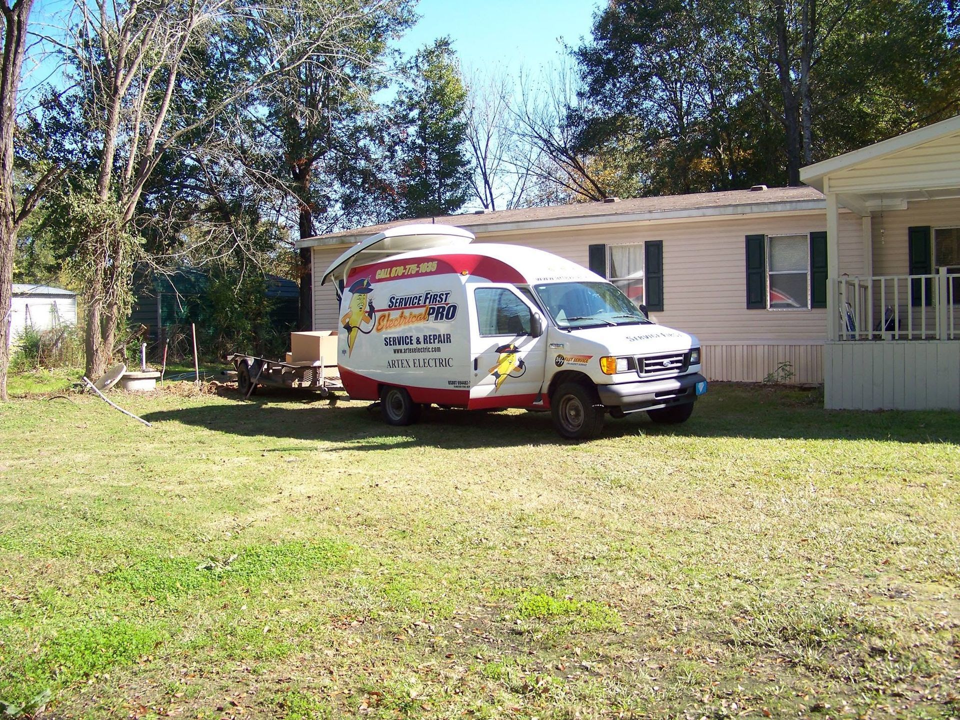 White service van parked on a grassy lawn beside a pink house and porch under trees