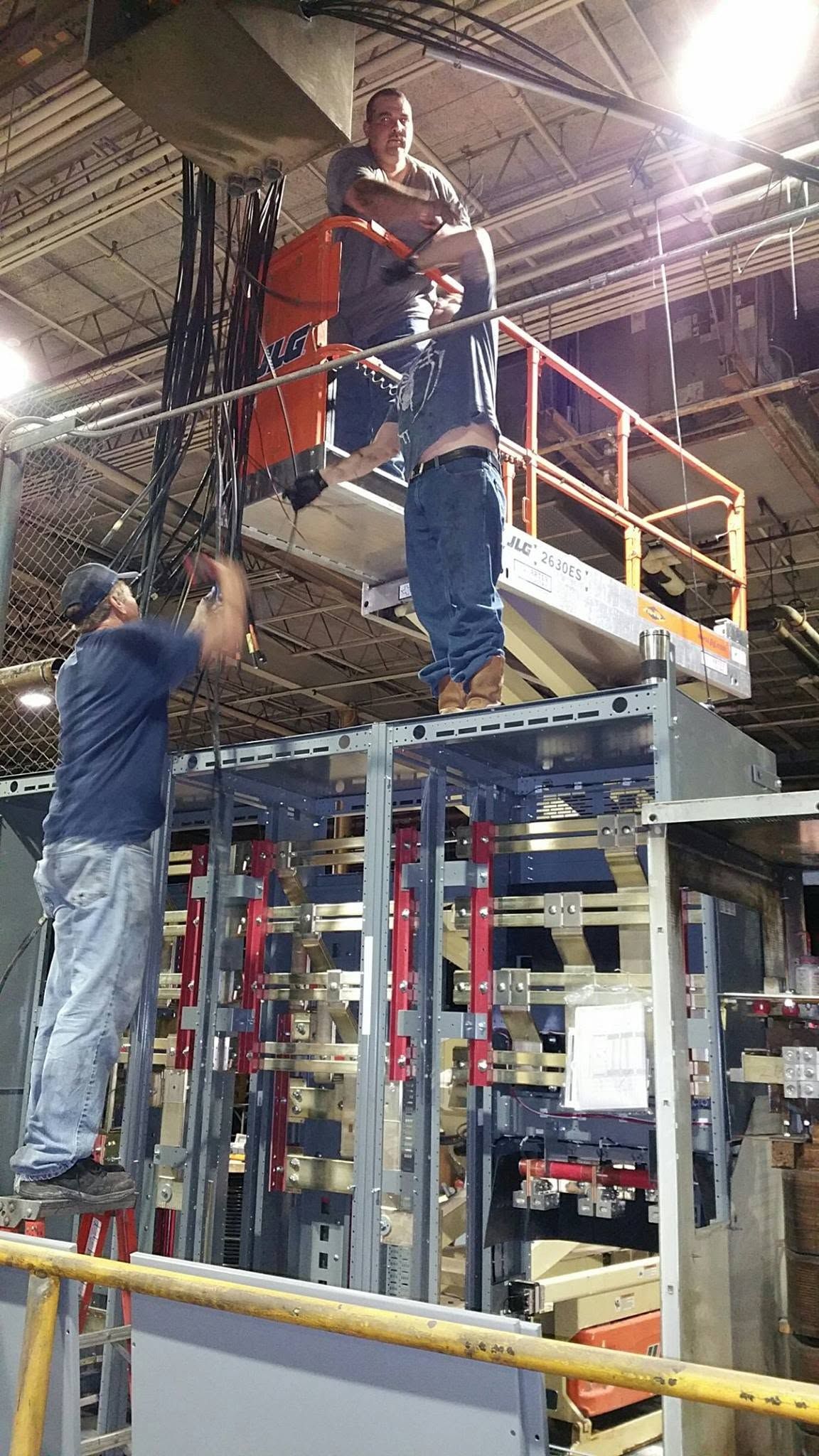 Workers assembling a scaffold platform in an industrial facility, with one worker on the upper level.