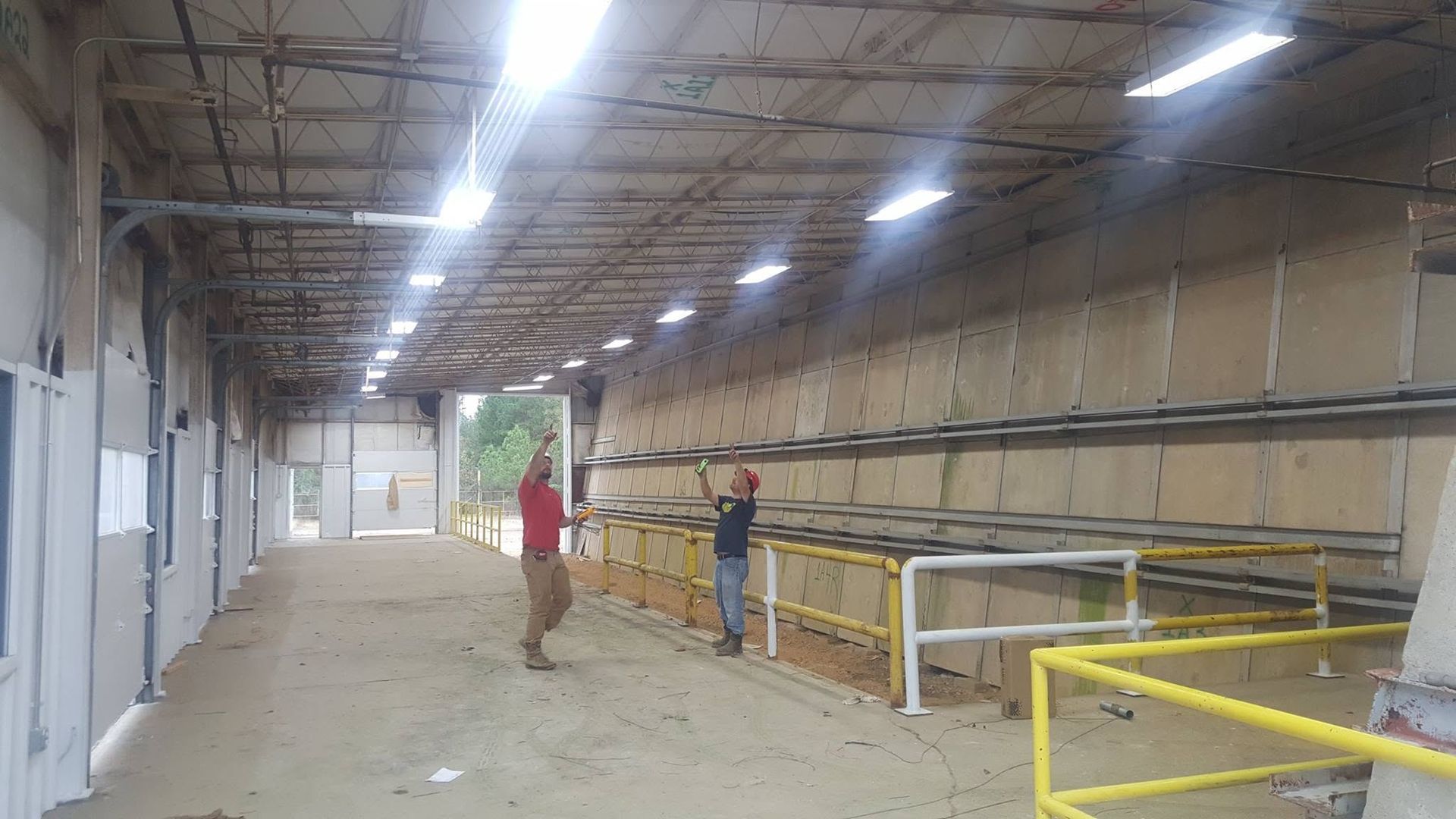 Industrial interior with two people standing on a raised walkway beside yellow railings and concrete walls