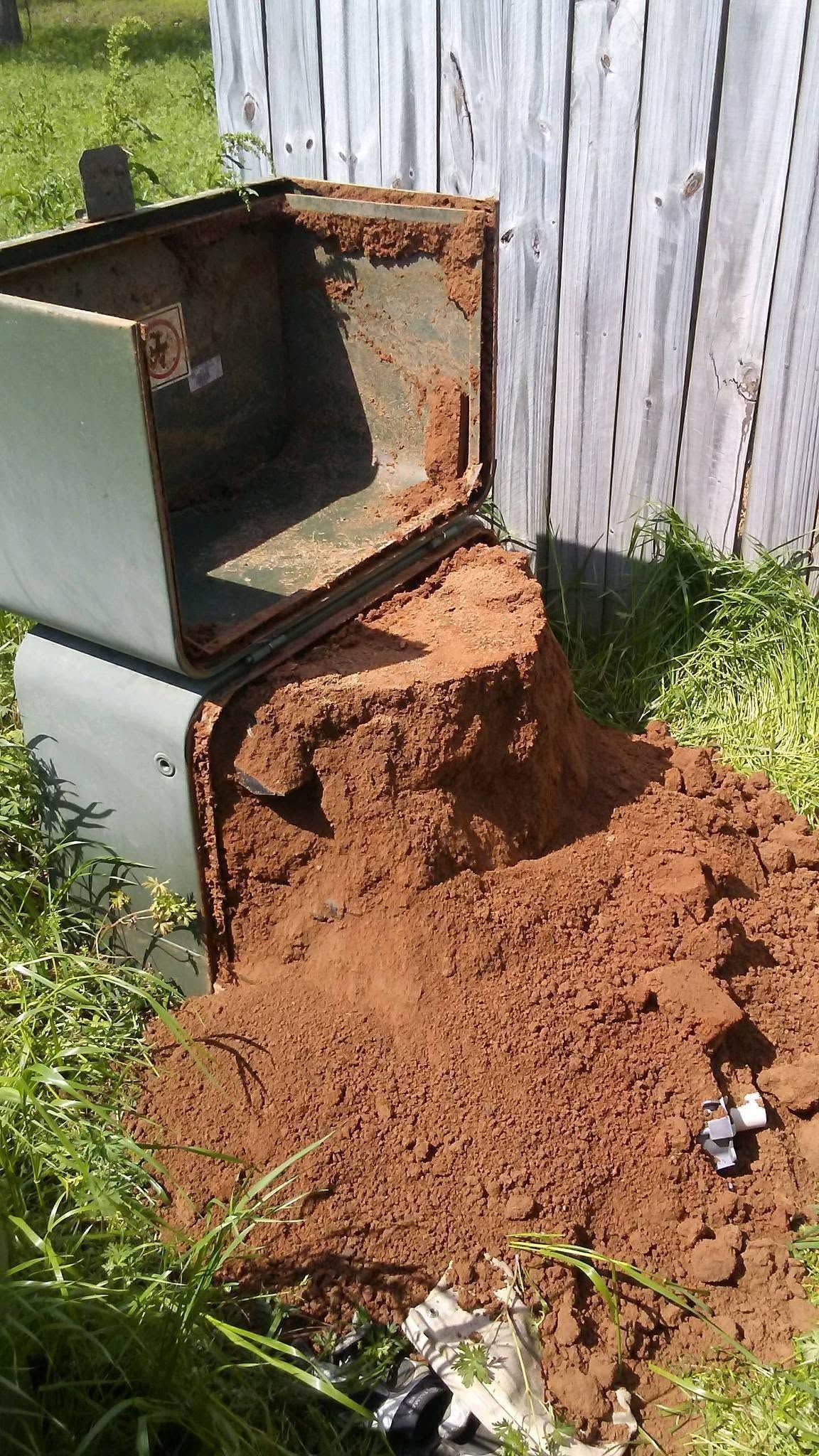 Open cabinet tipped onto dirt pile beside white fence and grass.