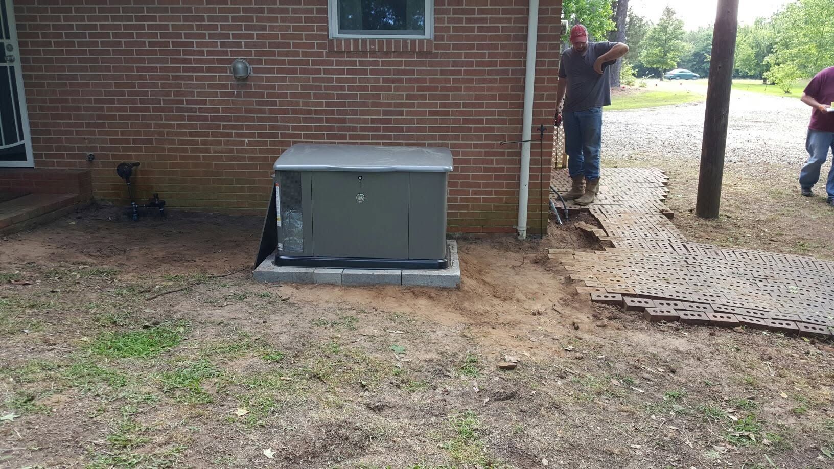 Outdoor electrical generator beside a brick building, with a person standing near the doorway.