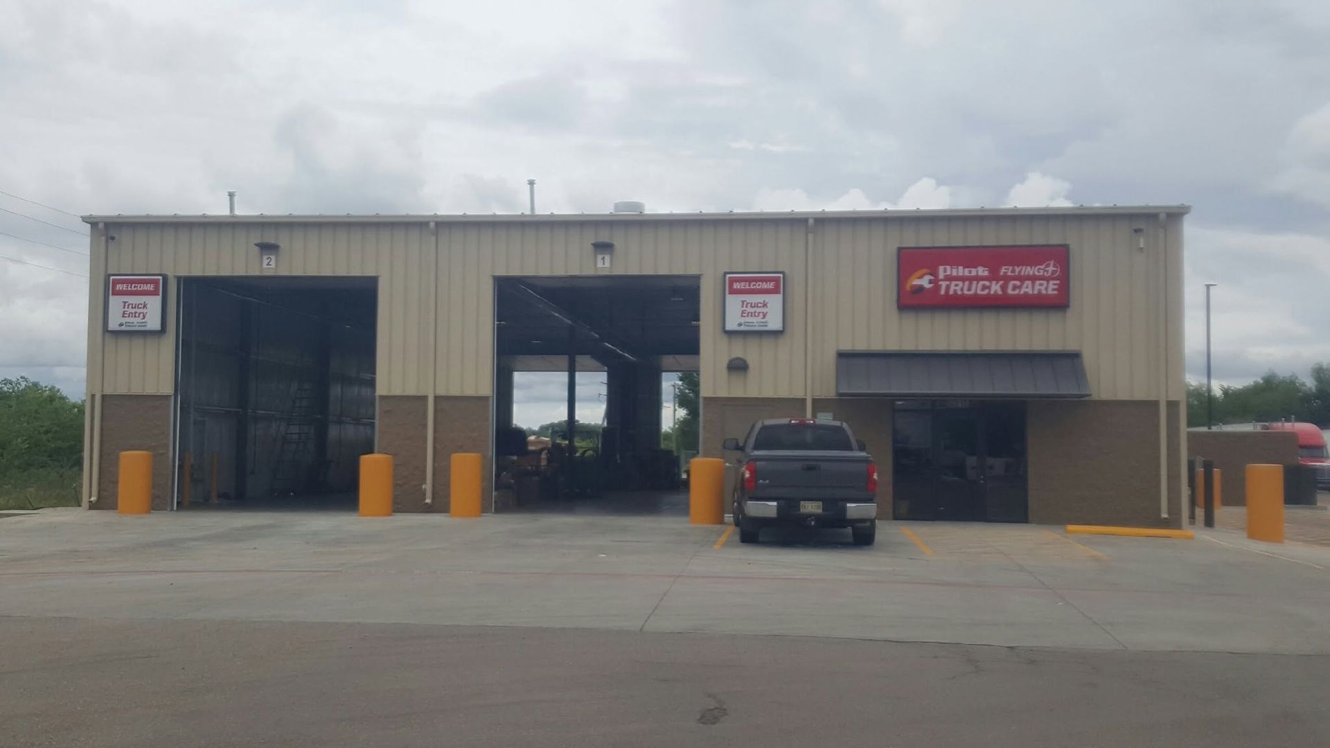 Small auto repair shop with open garage bays, red sign, and a parked pickup truck in front