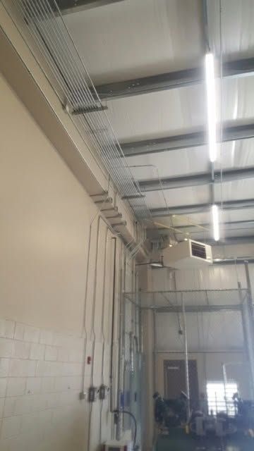 Industrial warehouse interior with ceiling lights, exposed pipes, and a high open doorway in the background