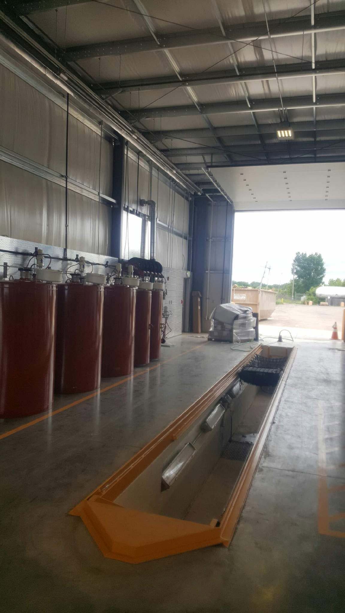 Industrial warehouse interior with red cylinders lined along a wall and a long floor trench in the center.