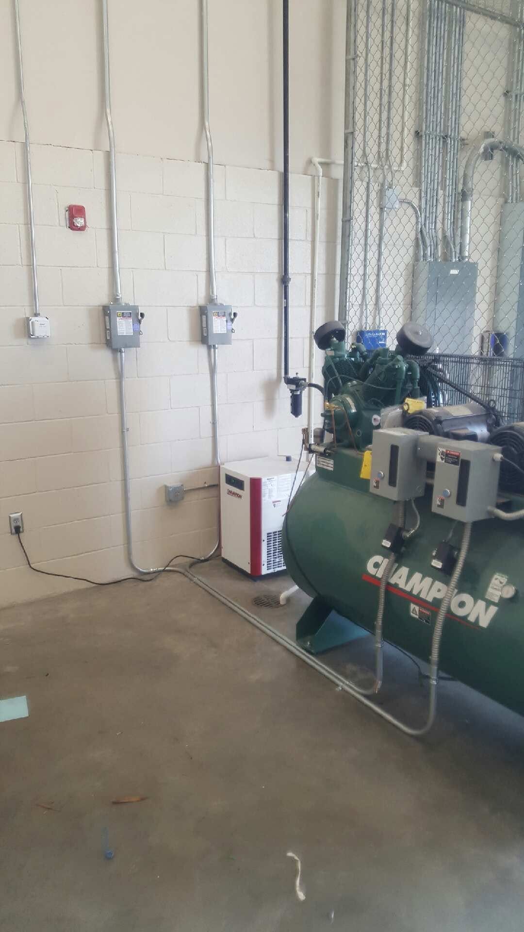 Industrial wall with electrical boxes, tall cables, and a green air compressor in a utility room