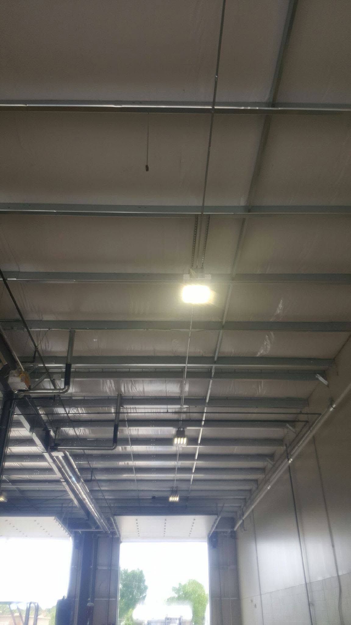 Interior of a warehouse loading bay with exposed steel beams, hanging lights, and an open doorway to daylight