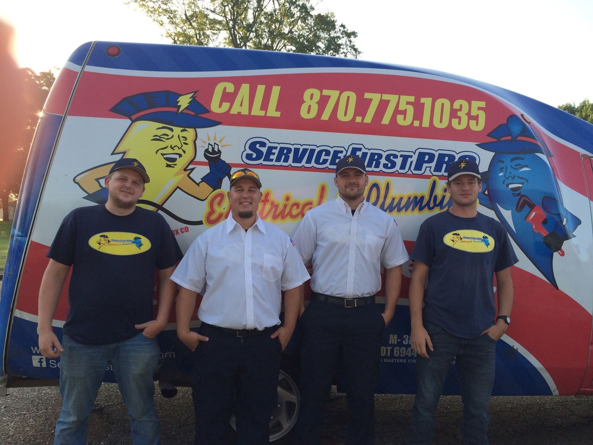 Four people posing in front of a Service First Plumbing truck with a large “CALL 870.775.1035” sign