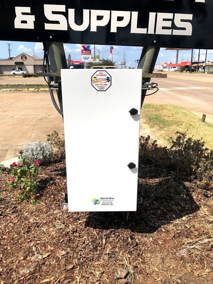 White outdoor utility cabinet in a landscaped roadside area beneath an 