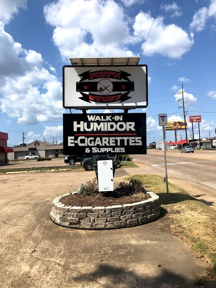 Walk-in Humidor Cigarettes & Supplies roadside sign on a stone base under a blue sky with clouds