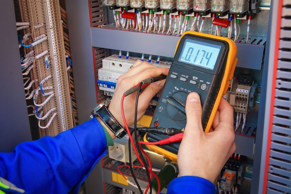 Technician testing an electrical control panel with a digital multimeter in a server room