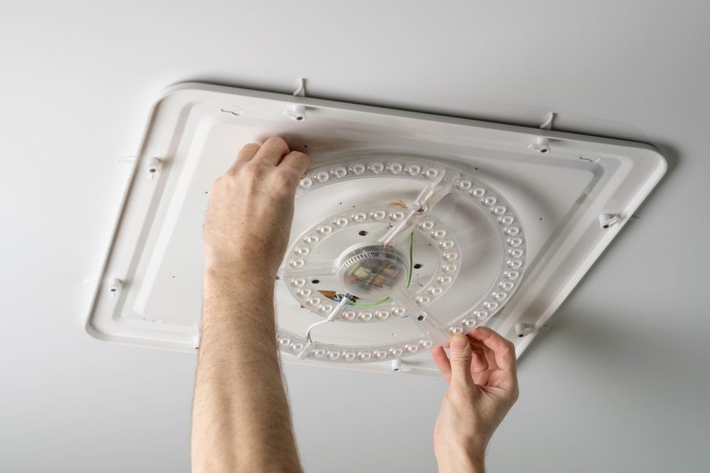 Hands installing a round LED ceiling light on a white ceiling panel